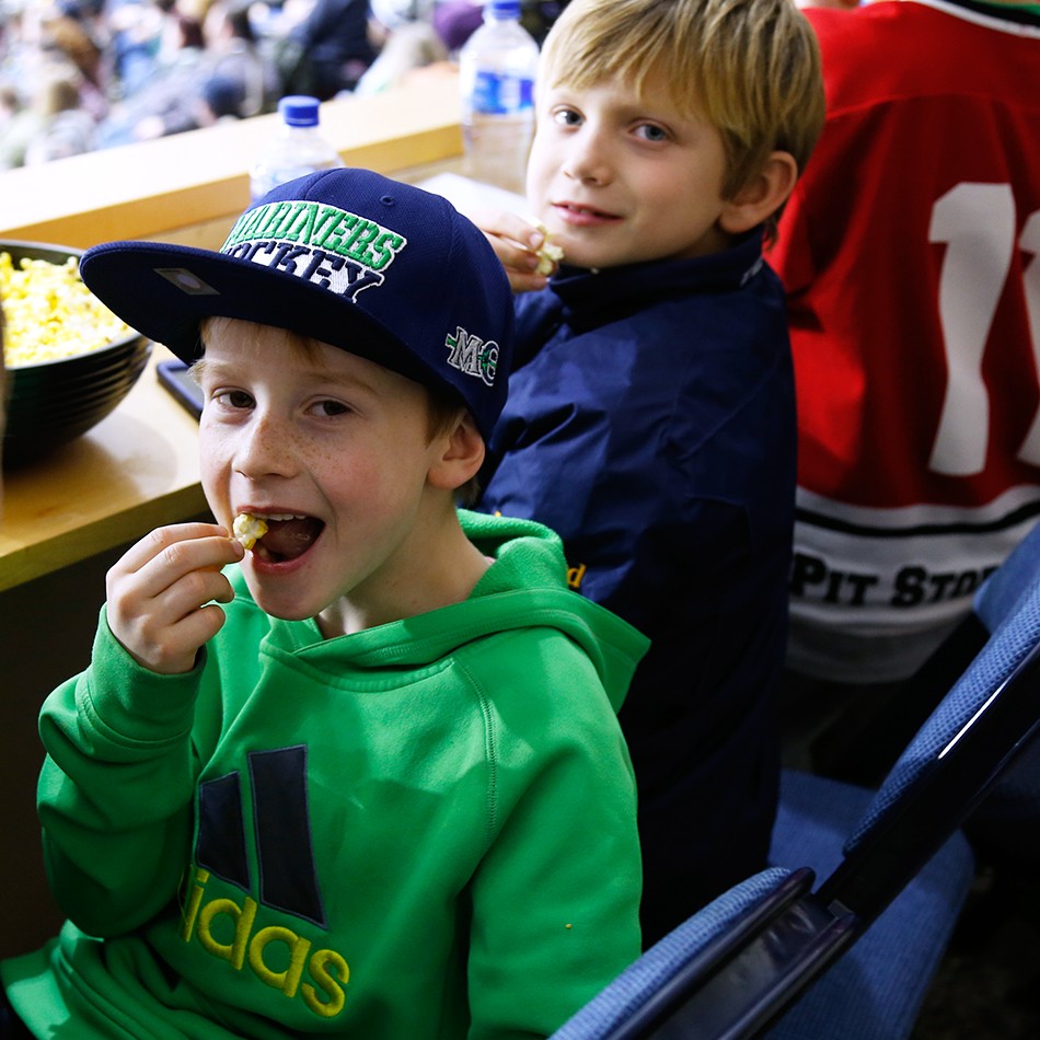 Child in Mariners hat enjoying popcorn during the game